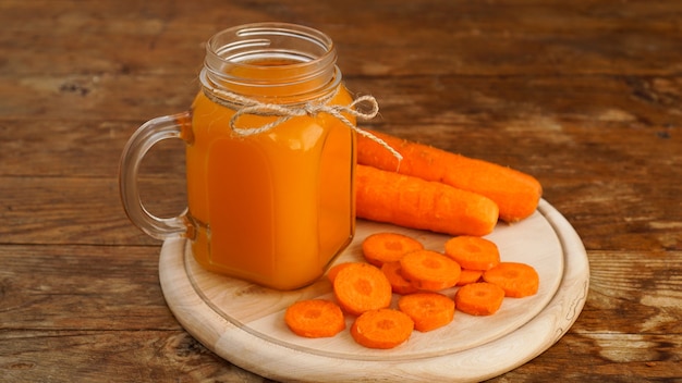 Jugo de zanahoria naranja brillante en un frasco de vidrio sobre un fondo de madera. Zumo y zanahorias picadas. Bebida casera con vitaminas