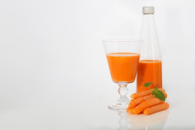 Jugo de zanahoria en un vaso y la botella y acostado junto a una zanahoria con menta