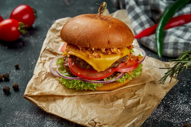 Jugosa hamburguesa doble con carne de res, tomates, queso y cebollas crujientes sobre una mesa oscura.