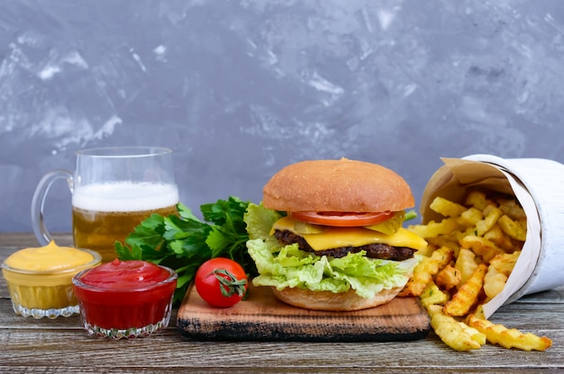 Foto jugosa hamburguesa, papas fritas, salsas, cerveza sobre un fondo de madera.