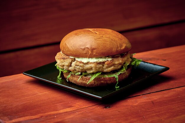 Jugosa hamburguesa de pescado con ensalada, queso, tomate y salsa. En un plato con patatas fritas. fondo de madera