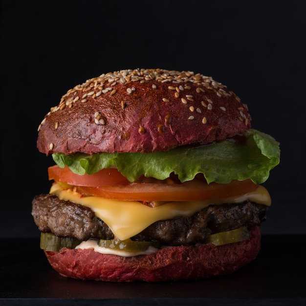 Jugosa hamburguesa con queso de pan rojo sobre un fondo negro, primer plano