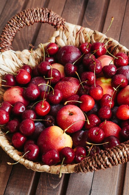 Jugosas cerezas y nectarinas en cesta en mesa de madera.