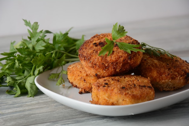 Jugosas chuletas de pollo fritas caseras. Rebozado con pan rallado, delicioso, en plato blanco con hierbas. Sobre fondo de madera vieja, estilo rústico