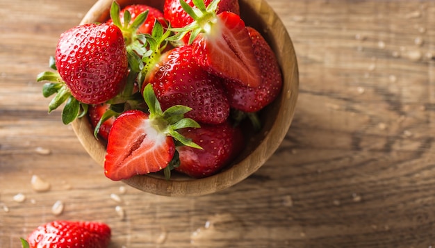 Jugosas fresas lavadas en un tazón de madera sobre la mesa de la cocina.