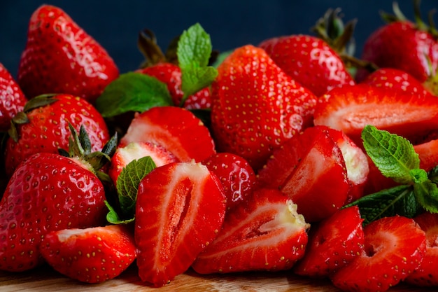 Jugosas fresas maduras enteras y cortadas sobre una tabla de madera