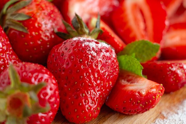 Jugosas fresas maduras enteras y cortadas sobre una tabla de madera