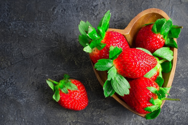 Jugosas fresas maduras en un tazón de madera en forma de corazón. Vista superior