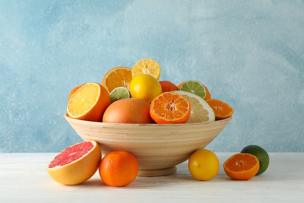 Jugosas frutas cítricas en un tazón en la mesa de madera sobre fondo azul, espacio para texto