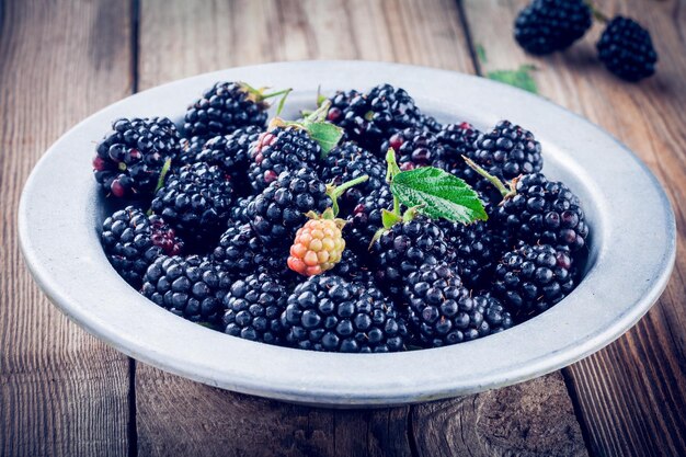 Jugosas moras orgánicas frescas en un tazón viejo sobre un fondo de madera