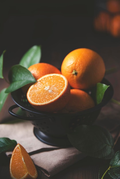 Unas jugosas naranjas en un recipiente negro con hojas verdes sobre un fondo de madera oscura. Concepto oscuro, rústico y de cerca.