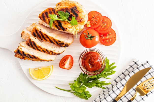 Jugosas porciones de filete de pollo a la parrilla en un plato de cerámica blanca con tomates cherry frescos vista superior menú de fondo blanco