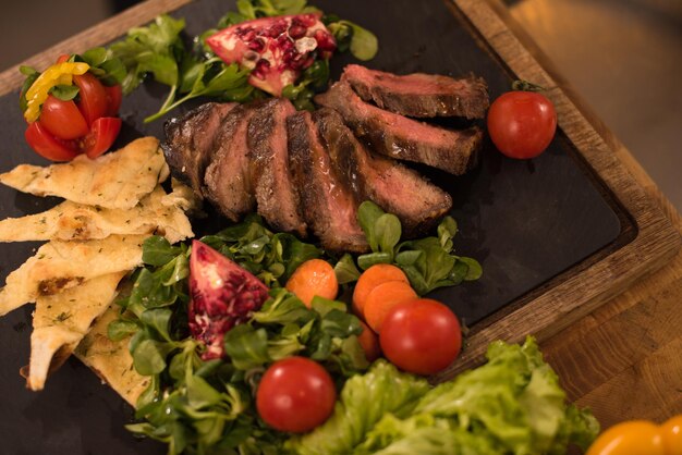 Jugosas rodajas de bistec a la parrilla con verduras sobre una tabla de madera