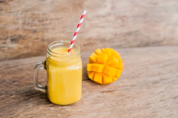 Jugoso batido de mango en frasco de vidrio con paja roja a rayas sobre fondo de madera vieja