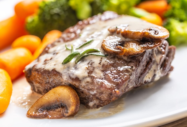 Foto jugoso bife de ternera con salsa de champiñones y verduritas.