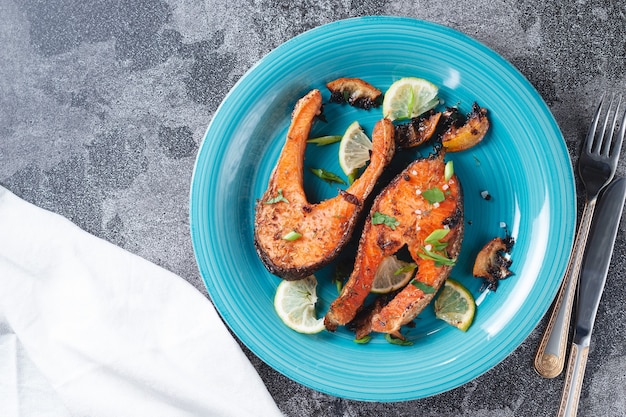 Jugoso filete de salmón a la parrilla con limón, especias y lima en un plato de pescado azul turquesa sobre una mesa de pizarra de piedra. Filete de salmón deliciosamente cocido