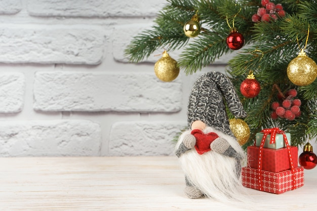 Juguete de año nuevo Santa Claus tiene corazón de forma roja sobre fondo de árbol de Navidad decorado