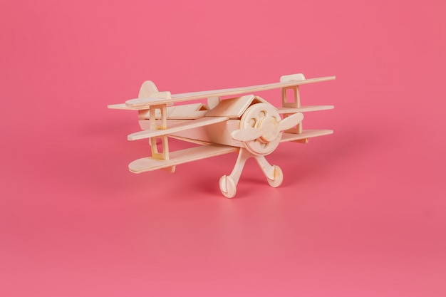 Juguete de avión de madera sobre un fondo rosa pastel