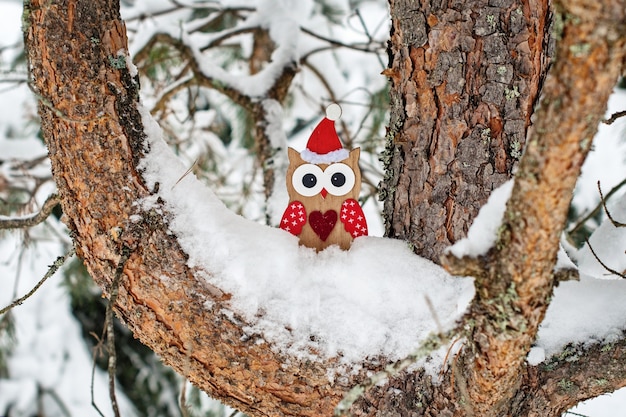 Juguete de búho de madera en traje de Santa en pino cubierto de nieve.