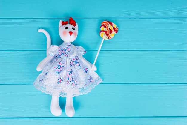 Juguete casero en forma de gato en un vestido sosteniendo piruletas de colores sobre tablero de madera turquesa