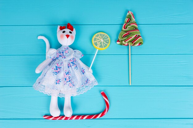 Juguete casero en forma de un gato con un vestido en el trineo de caramelos con piruletas de colores sobre tablero de madera turquesa