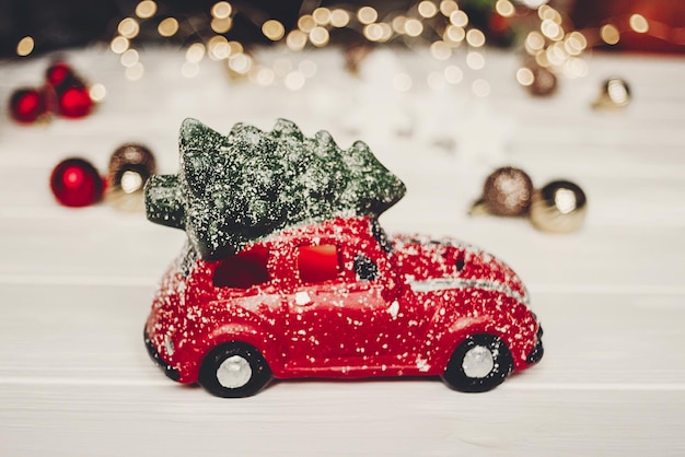 Juguete de coche rojo de regalo de navidad con árbol de navidad en la parte superior de madera blanca con luces en el espacio de fondo para texto saludos de temporada felices fiestas regalo de navidad celebración navideña