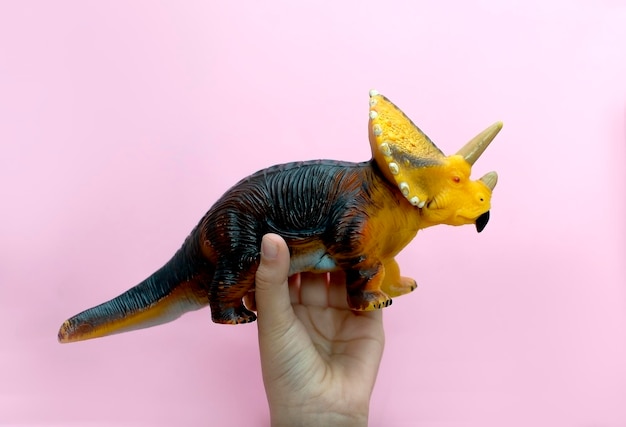 Foto juguete de dinosaurio de plástico sobre fondo rosa un niño de 57 años sostiene un dinosaurio de plástico