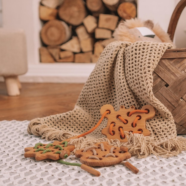 Juguete de madera para niños con agujeros para atar con cordón naranja sobre manta beige sobre fondo de chimenea. Marco cuadrado