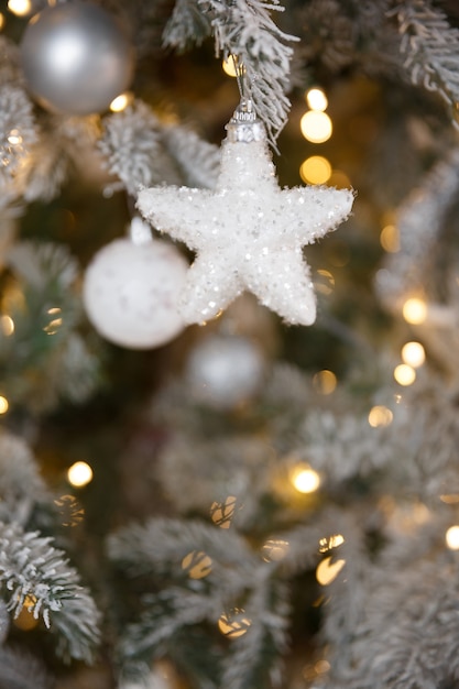 Juguete de Navidad blanca colgando de una rama de abeto nevado verde, primer plano