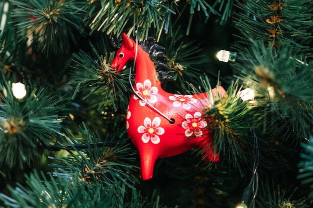 Juguete de navidad rojo en forma de caballo con flores en un primer plano de árbol de navidad