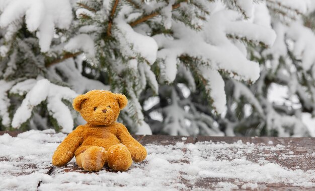 Juguete del oso de peluche en la nieve en la mesa de madera junto al pino