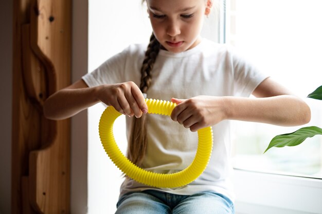 Juguete plástico de tubo de pop sensorial antiestrés en manos de un niño. una niña pequeña feliz juega con un juguete poptube fidget en casa. niños sosteniendo y jugando pop tube color amarillo, tendencia 2021 año