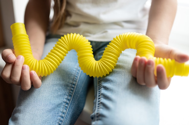 Juguete plástico de tubo de pop sensorial antiestrés en manos de un niño. una niña pequeña feliz juega con un juguete poptube fidget en casa. niños sosteniendo y jugando pop tube color amarillo, tendencia 2021 año