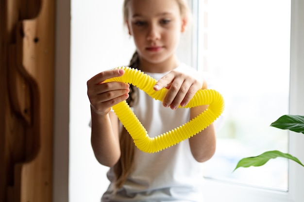 Juguete plástico de tubo de pop sensorial antiestrés en manos de un niño. una niña pequeña feliz juega con un juguete poptube fidget en casa. niños sosteniendo y jugando pop tube color amarillo, tendencia 2021 año