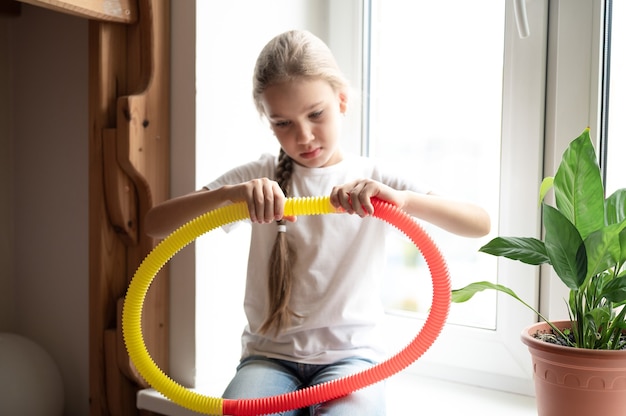 Juguete plástico de tubo de pop sensorial antiestrés en manos de niños. una niña pequeña feliz juega con un juguete poptube fidget en casa. niños sosteniendo y jugando pop tube color amarillo y rojo, tendencia 2021 año