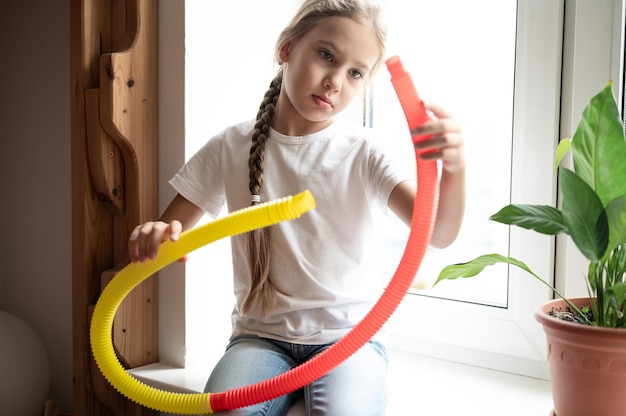 Juguete plástico de tubo de pop sensorial antiestrés en manos de niños. una niña pequeña feliz juega con un juguete poptube fidget en casa. niños sosteniendo y jugando pop tube color amarillo y rojo, tendencia 2021 año