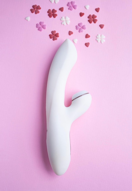 El juguete vibrador blanco para adultos se encuentra sobre un fondo rosa junto a corazones decorativos que imitan un orgasmo Fotografía conceptual