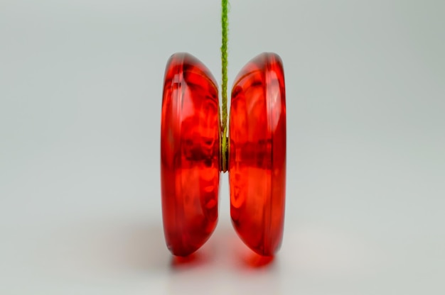 Juguete yo-yo de plástico rojo aislado sobre fondo blanco con una cuerda verde atada a él.