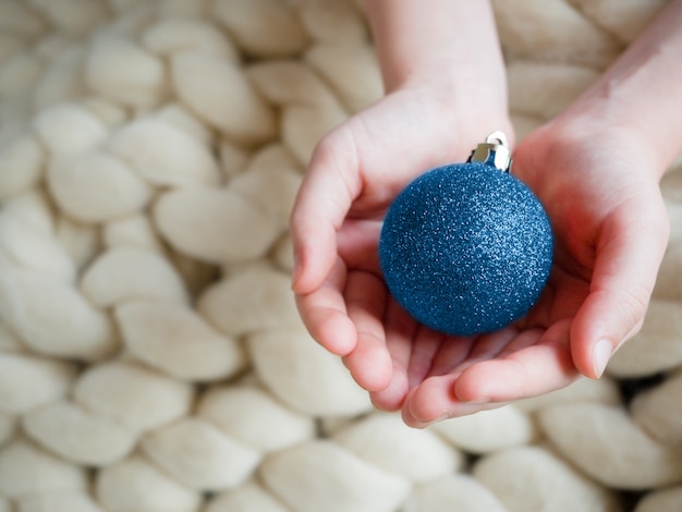 Juguetes de árbol de Navidad como bola azul en manos en vista superior de lana