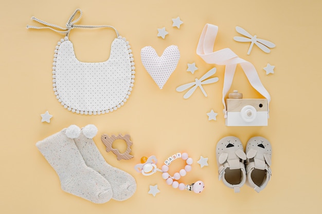 Foto juguetes, babero, calcetines, zapatillas para recién nacido sobre fondo amarillo. marco hecho de artículos y accesorios para bebés de género neutro. endecha plana, vista superior