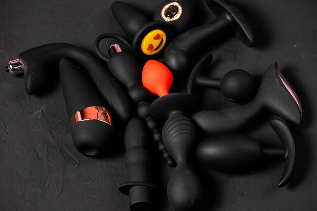 Juguetes eróticos de placer sobre un fondo negro Aparatos sexuales y dispositivos de masturbación Consolador rosa rodeado de goma negra y juguetes sexuales de silicona tapones anales vibradores bolas vaginales Vista superior