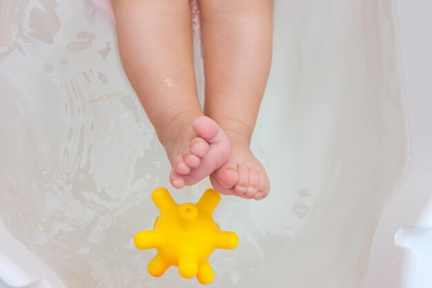 Juguetes de goma en la bañera con pies de bebé.