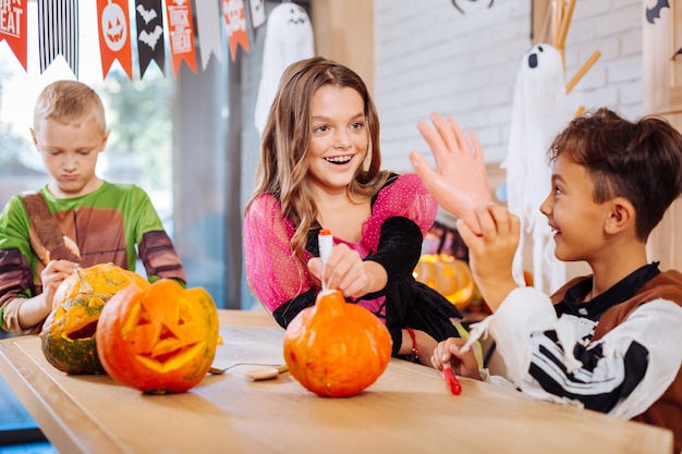 Juguetes de Halloween. Tres niños vestidos con bonitos disfraces que se sienten graciosos mientras sostienen juguetes de Halloween para la fiesta