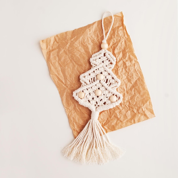 Juguetes de macramé de árbol de Navidad en papel artesanal Fondo blanco Materiales naturales hilo de algodón perlas de madera y palo Decoraciones ecológicas adornos decoración hecha a mano Vacaciones de invierno y año nuevo