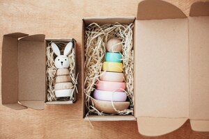 Foto juguetes de madera con estilo para niños en una caja artesanal sobre una mesa de madera pirámide de madera moderna y colorida con anillos en colores del arco iris y conejito juguetes ecológicos sin plástico para niños pequeños