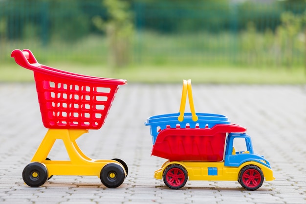 Juguetes de plástico de colores brillantes para niños al aire libre en un día soleado de verano. Camión, cesta y carretilla de compras.