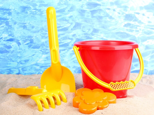 Juguetes de playa para niños en arena sobre fondo de agua
