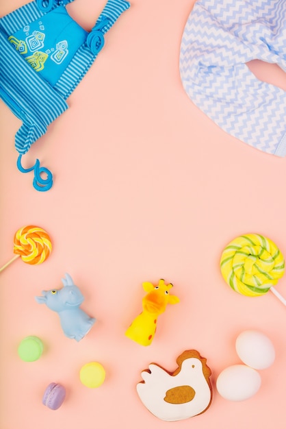 Foto los juguetes y la ropa del bebé se presentan sobre un delicado fondo rosa. pan de jengibre festivo en forma de pollo, dos huevos blancos y dulces. concepto de infancia.