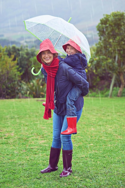 Juguetón bajo la lluvia Retrato recortado de una madre que lleva a su hijo de espaldas afuera bajo la lluvia