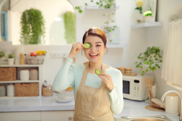 Juguetonamente cubriendo un ojo con una rodaja de pepino, sonriendo mirando a la cámara